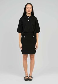 Polo noir en tricot à manches courtes avec trois boutons associé à une jupe crayon noire en tricot dotée de poches décoratives et de boutons.