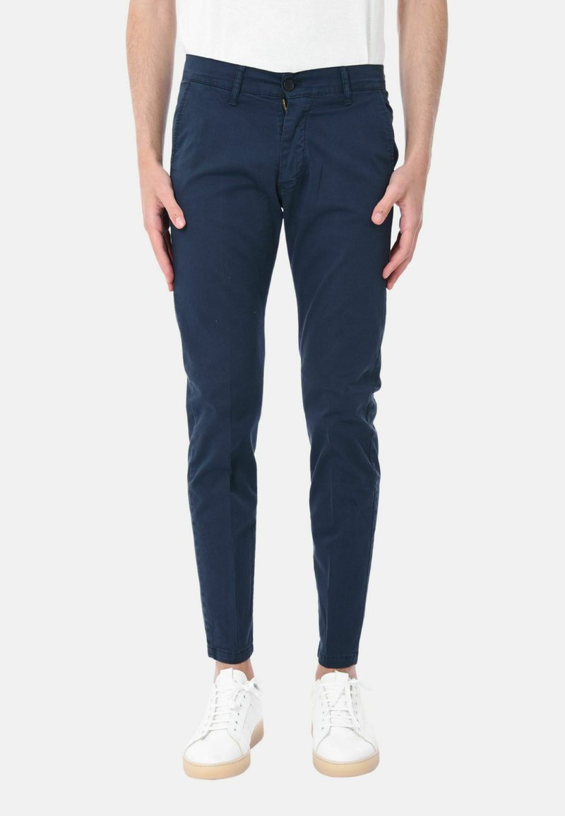 Chino blu navy in cotone, con design slim fit, tasche frontali e chiusura con bottone e cerniera, abbinati a sneaker bianche.