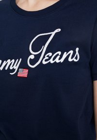 Námorně modré bavlněné tričko s bílým vyšívaným nápisem "my Jeans" a malou červenou a modrou vlajkovou nášivkou na levé straně. Krátké rukávy.