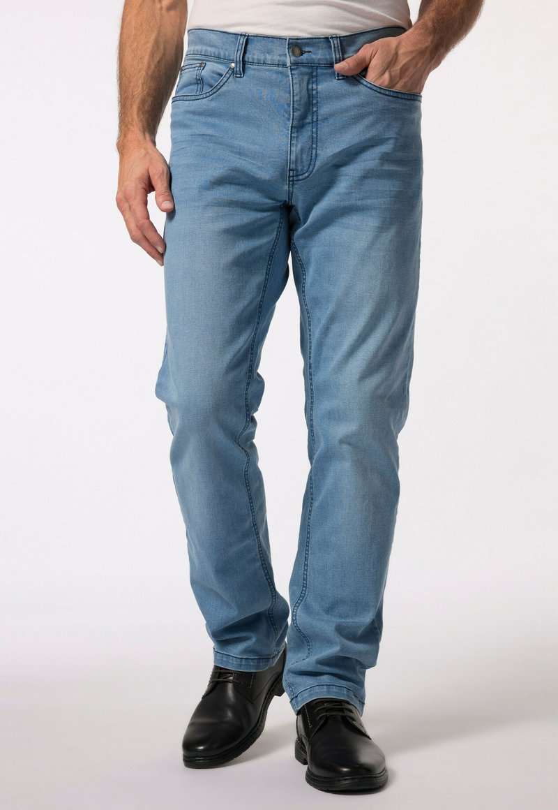 Světle modré džínové kalhoty slim fit s pěti kapsami a zipovým zavíráním. Oblečené s černými lesklými botami, které mají hladkou texturu.