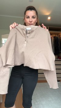 Top a maniche lunghe cropped color beige in tessuto testurizzato, colletto henley con bottoni e maniche ampie. Abbinato a pantaloni neri attillati.