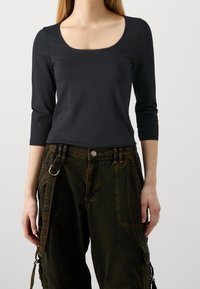 Black long-sleeve top with a rounded neckline, paired with dark green cargo pants featuring multiple pockets and a side strap detail.