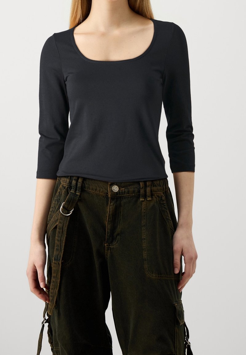 Black long-sleeve top with a rounded neckline, paired with dark green cargo pants featuring multiple pockets and a side strap detail.