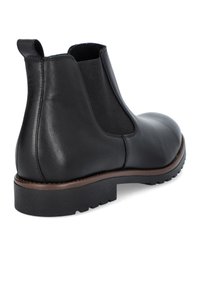 Czarne skórzane botki Chelsea z elastycznymi bocznymi panelami, okrągłym noskiem i niskoprofilową gumową podeszwą z brązowym akcentem wokół podstawy.