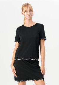 Femme portant un ensemble haut à manches courtes noires et jupe avec des bordures en sequins argentés découpés, posant devant un fond blanc.