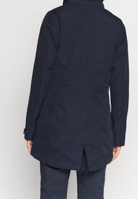 Chaqueta impermeable de color navy con capucha, costuras reforzadas y un respiradero en la parte posterior para ventilación. Textura suave y puños ajustables.