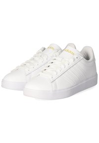 Biele tenisky vyrobené z hladkého syntetického materiálu, s tromi diagonálnymi pruhmi, plochými šnúrkami a polstrovaným golierom. Zlaté logo na jazyku.