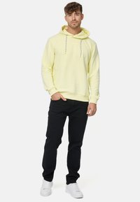 Sudadera amarilla con capucha y cordones ajustables, combinada con jeans negros y zapatillas blancas. Material de mezcla de algodón suave.