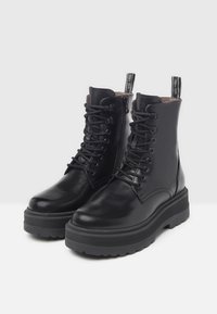 Schwarze Leder-Stiefeletten mit Schnürung, Seiteneingriff, runder Zehenpartie und dicker Gummisohle. Besitzt eine strukturierten Oberfläche und eine Ziehschlaufe.