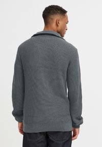Grå strikket cardigan med sjalkrage, med ribbestruktur, lange ermer og løs passform. Synlige sømdetaljer.