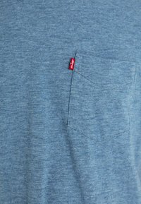 Kék melírozott póló, amelyen mellzseb található, puha anyagból készült. A zseb közepén egy kis piros Levi's logó címke található, ami részletgazdagabbá teszi.