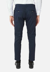 Chino blu navy con una vestibilità slim, due tasche posteriori con chiusura a bottone e una superficie in cotone liscia. Indossati con scarpe nere.