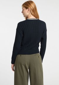 Marinblå ribbad tröja med rund halsringning, med en kontrasterande vit kant vid kragen. Matchas med olivgröna vida byxor.