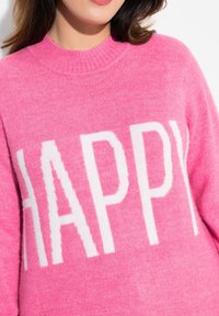 Gestrickter Pullover in leuchtendem Pink mit geripptem Ausschnitt; verfügt über großen weißen Text "HAPPY" auf der Vorderseite. Weiche Textur.