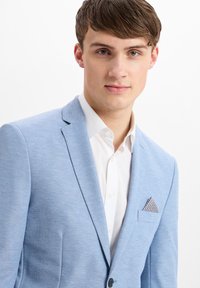 Helles blaues strukturiertes Blazer mit einem einzigen Knopf, Reverskragen und einem Einstecktuch mit geometrischem Muster; getragen über einem weißen Hemd.