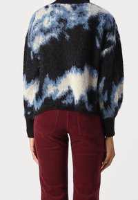 Ein oversized gestrickter Pullover in Schwarz, Blau und Creme mit strukturiertem Finish, kombiniert mit burgunderfarbener Cordhose.