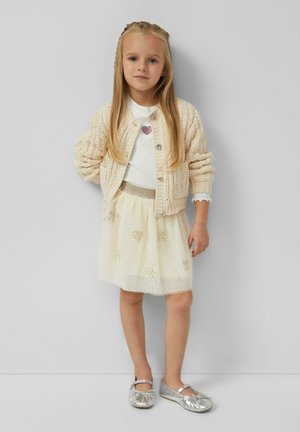 Cream knitted cardigan, white shirt with heart design, layered tulle skirt with gold details, and silver ballet flats.