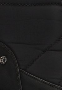 Tela negra acolchada con una textura suave, con herrajes plateados y detalles de costura en contraste. Acentuada con un emblema de logo redondo.