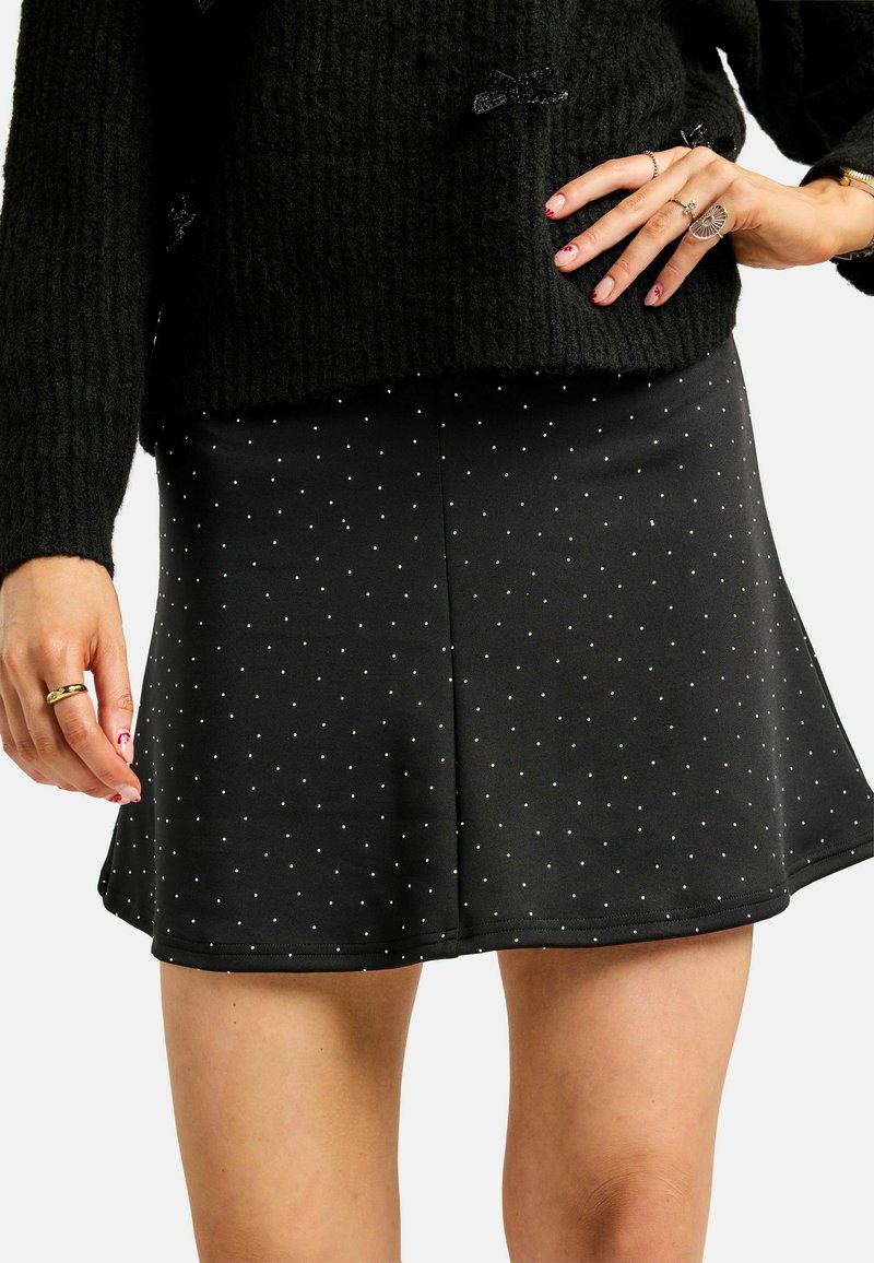 Černá rozšířená sukně z elastické látky s bílými puntíky. Má elastický pas a hladkou texturu, sahá nad polovinu stehna.