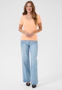 T-shirt rosa con coste, maniche corte e dettaglio in pizzo lungo il collo, abbinato a jeans svasati azzurri e scarpe nere a punta.