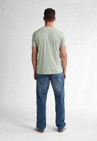 Camiseta de manga corta verde claro con cuello redondo, combinada con jeans de mezclilla azul de corte suelto. Costuras visibles y bolsillos traseros.