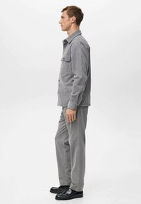 Ensemble chemise et pantalon en velours côtelé gris, avec une fermeture à boutons, des poches latérales et des chaussures plates. Texture lisse avec des lignes verticales.