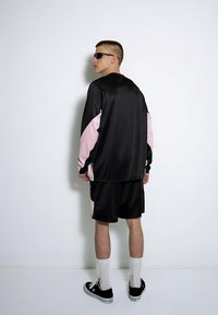 Czarny strój sportowy z fakturowaną, długą koszulką z różowymi akcentami i dopasowanymi szortami, uzupełniony białymi skarpetkami i czarnymi butami.