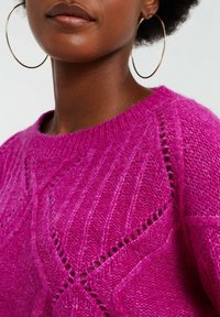 Fuchsiový pletený svetr s texturovaným vzorem ve tvaru diamantů a otevřenými stehy, kulatým výstřihem a měkkým, načechraným vzhledem.
