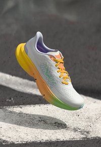 Baskets de course blanches avec une tige texturée, des lacets jaunes et une semelle dégradée multicolore. Présente le logo "HOKA" en teal.