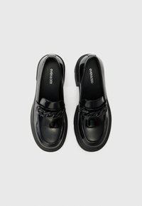 Mocassins en cuir verni noir avec une semelle épaisse, ornés d'une chaîne décorative et d'une texture lisse sur le dessus.