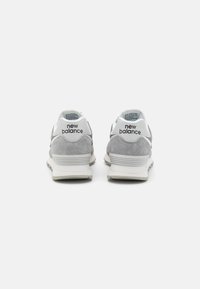 Dvojice šedobílých tenisek New Balance z pohledu zezadu na bílém pozadí.