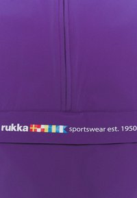 Top sportivo viola con zip centrale, caratterizzato da testo bianco e un logo colorato nella parte inferiore. Texture liscia e design moderno.