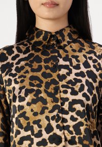 Leopard print blouse features a collared neckline, long sleeves, and black buttons on a silky fabric with a smooth texture.