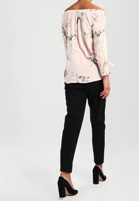 Blusa rosa floreale off-the-shoulder con maniche larghe, abbinata a pantaloni neri aderenti e scarpe con tacco nere.