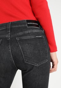 Svarta denimjeans med en figurnära design, som har en märkesresår i midjan, två bakfickor och synliga sömmar.