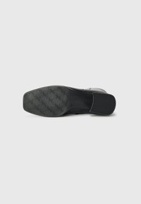 Suela de zapato negra con una superficie de goma texturizada que presenta un patrón ondulado y un tacón cuadrado. Nombre de la marca "Gabor" grabado en el lado.