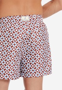 Bruna badshorts med ett geometriskt mönster av vita diamanter och blå accenter. Elastisk midja med en etikett märkt "Garcia Amore."}}}