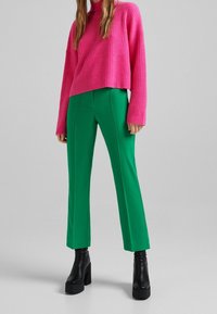 Rosa ribbad tröja med långa ärmar, matchad med gröna tajta byxor. Svarta klackstövlar med blockklack fulländar hela outfiten.