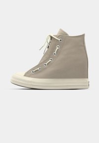 Beige lerret høyhælte sneakers med rund tå, kremfarget gummisåle, sølvfargede metallringer og hvite lisser, med en teksturert overflate.