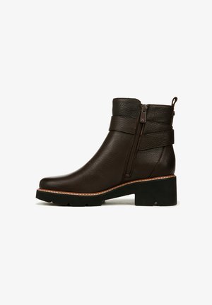 Bottines en cuir marron avec une finition texturée, fermeture éclair sur le côté, deux accents de sangle et un talon épais noir. Bordure blanche cousue autour de la semelle.