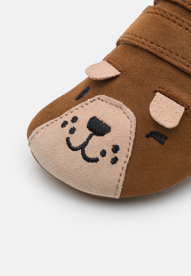 Braune Wildlederschuhe mit einem Hundegesicht-Design, einer beige Vorderseite und schwarzen bestickten Details. Mit verstellbaren Klettverschlüssen.