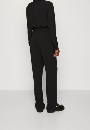 Pantalones negros de corte holgado con cintura alta, hechos de tela suave. Presentan una pretina fruncida y un diseño de pierna recta.