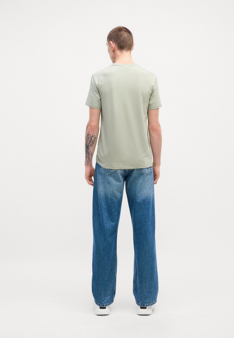 Light green short-sleeve t-shirt, smooth texture, paired with loose-fitting blue denim jeans featuring a gradient wash and white sneakers.