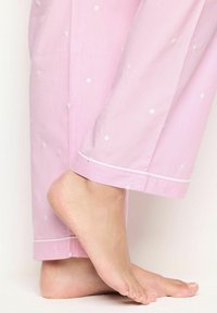 Roze stoffen pyjamabroek met witte stippen, een streeppatroon en witte afwerking. De onderkant reikt tot halverwege de enkel, zodat een blote voet zichtbaar is.