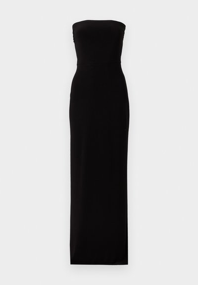 Μακρύ, μαύρο βραδινό φόρεμα χωρίς τιράντες με εφαρμοστή μπούστα και ίσια σιλουέτα σε απλό φωτεινό φόντο.