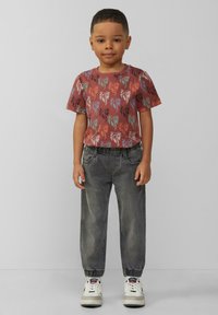 Camisa de manga corta con patrón de palmeras en rojo y verde, combinada con joggers gris ajustados y zapatillas blancas con detalles en negro.