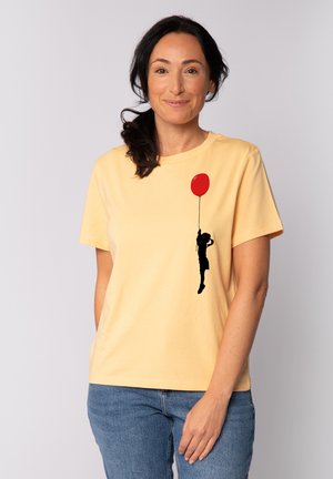 Gelbes Baumwoll-T-Shirt mit schwarzer Silhouette einer Person, die einen roten Ballon hält. Kurze Ärmel und runder Halsausschnitt. Lässige Passform.