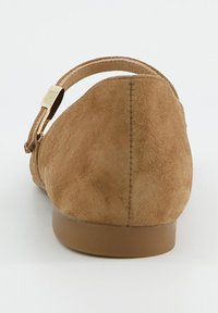 Hnědá semišová balerína s kulatou patou, nízkým podpatkem a nastavitelným páskem kolem kotníku se zlatými kovovými doplňky.