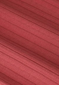 Textielstof in diep rood met subtiele gestructureerde strepen. Bevat delicate stikdetails die parallel lopen, waardoor een gelaagd uiterlijk ontstaat.