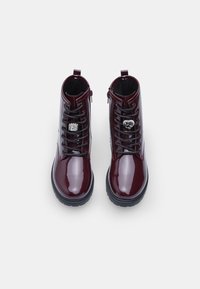 Stivaletti in pelle patinata bordeaux con lacci neri, decorazioni laterali e suole in gomma nera spessa.